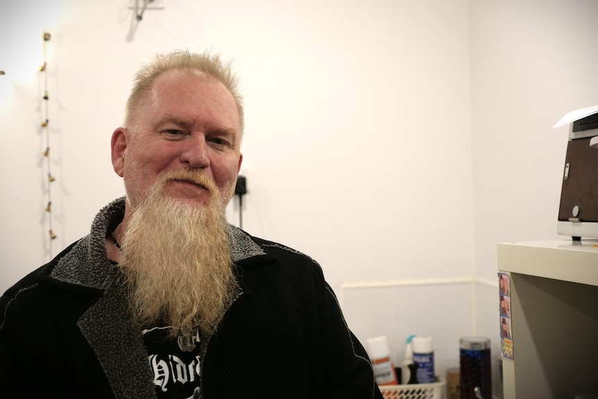 A man with a beard wears a black jacket in a room.