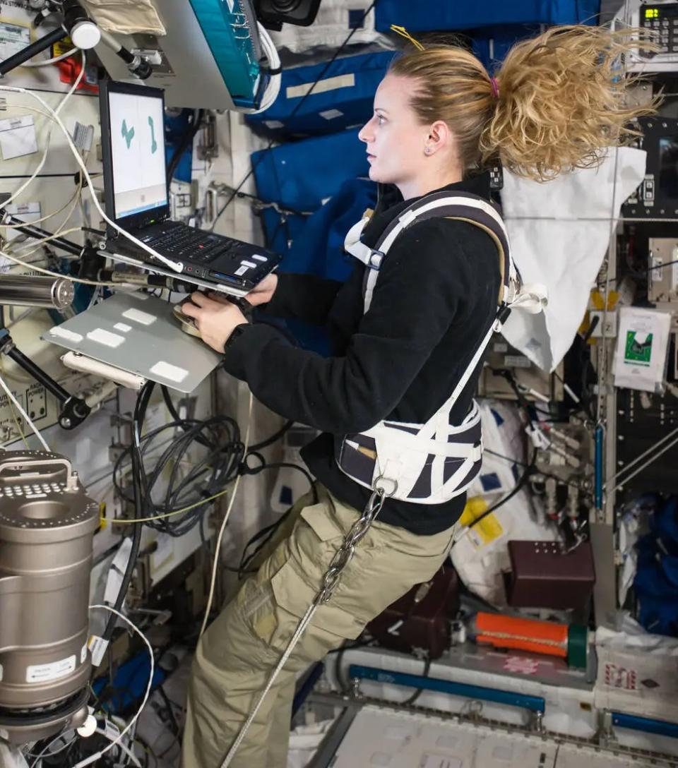 An astronaut looks at a computer screen while walking in a model of the space station