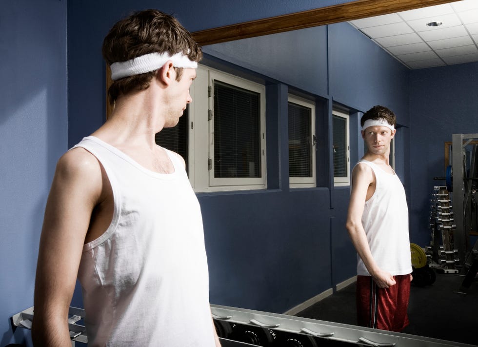 Man in sweatpants looking at reflection in gym mirror, shaking hands