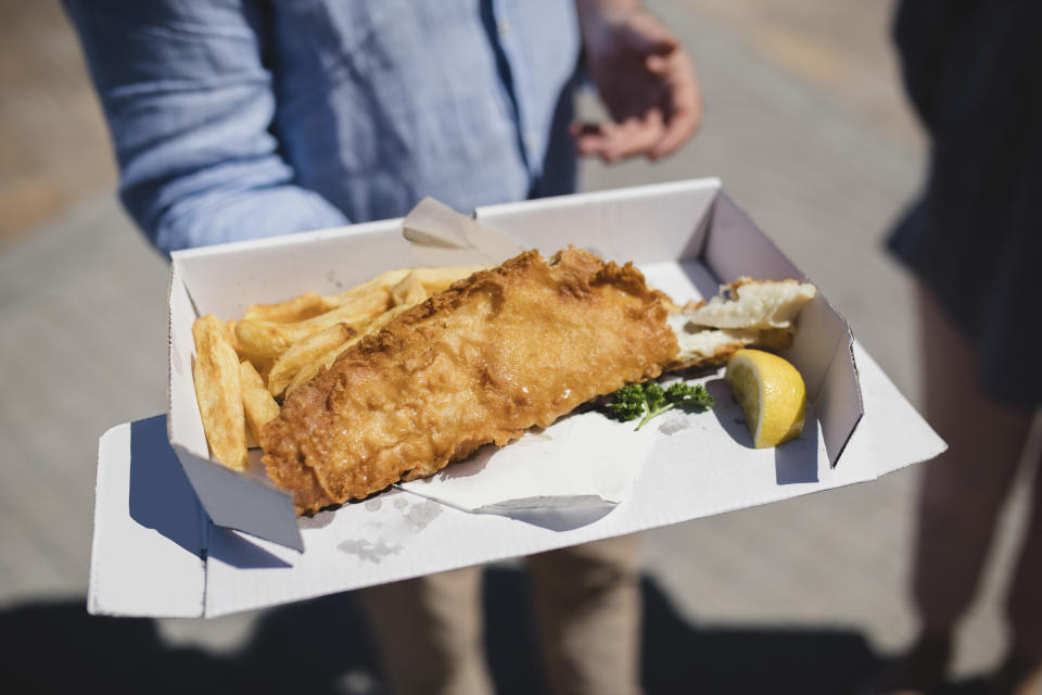 Person holding a cardboard box with battered fish and chips, traditionally British, British food, takeaway